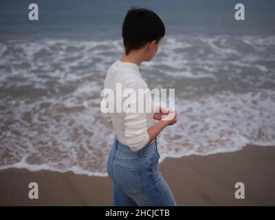 woman standing in front of the sea watching the waves move Stock Photo