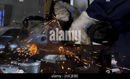 Male hand cuts off pieces of water pipe with angle grinder. Cutting of a steel with splashes of sparks at construction site. Sparks during cutting of Stock Photo