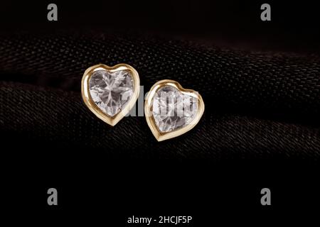 Hearts-shaped golden stud earrings on black fabric background. Stock Photo