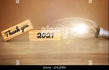 Image with thank you 2021 text on wooden blocks with bright light bulb background. Stock Photo