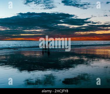 Silhouette of three people enjoying late sunset at west coast beach, California Stock Photo
