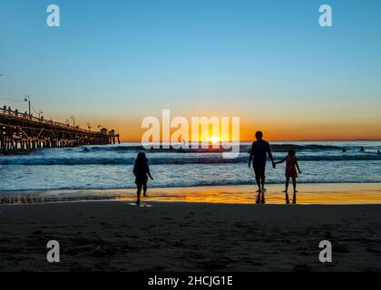 Silhouette of two kids and an adult enjoying late sunset walks at the seashore Stock Photo