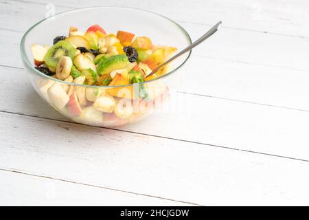 Studio shot of glass bowl with freshly made fruit salad in it on a white wooden table. Healthy eating concept. Vegetarian food. Vegan raw diet Stock Photo