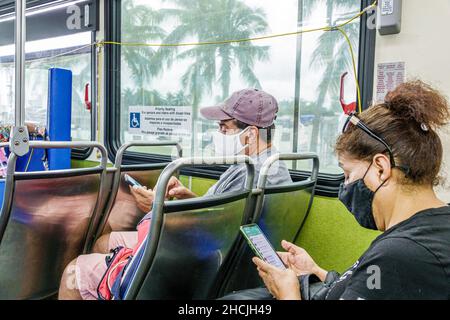 Miami Beach Florida Miami-Dade Metrobus 120 onboard passengers riders wearing face mask masks man Hispanic woman inside interior bus public transporta Stock Photo