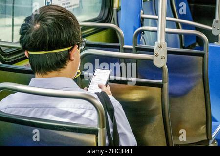 Miami Florida Miami-Dade Metrobus onboard passenger rider wearing face mask man inside interior bus public transportation using reading texting messag Stock Photo