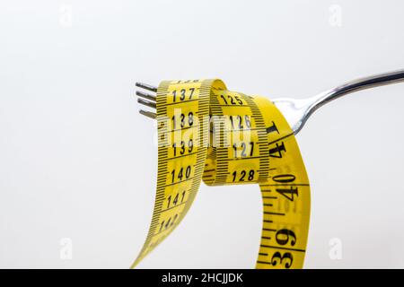 Fork with a measuring tape as if it were pasta, concept for a slimming diet, isolated on a light gray background, copy space, selected focus, narrow d Stock Photo