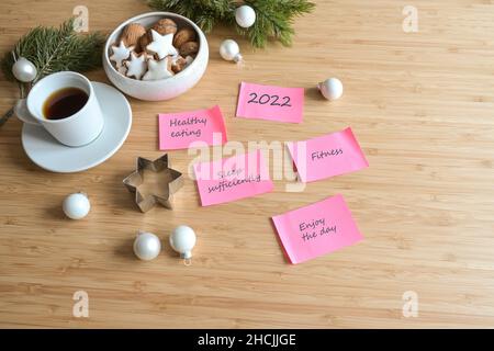 Pink sticky notes with goals and resolutions for the new year 2022 on a wooden desk with coffee, cookies and fir branches, copy space, selected focus Stock Photo