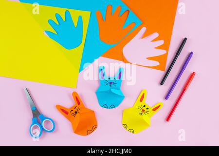 DIY and kids creativity. Colorful paper bunnies from childrens palm of their hand. Greeting cards with bunny on pink background. Gift idea, decor Spring, Easter. Process kid children craft. Stock Photo