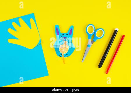 DIY and kids creativity. Colorful paper bunnies from childrens palm of their hand. Greeting cards with bunny on yellow background. Gift idea, decor Spring, Easter. Process kid children craft. Top view. Stock Photo