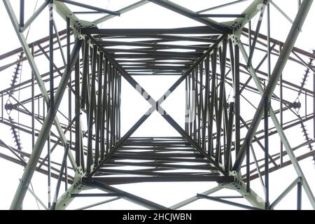 Photograph looking up internally through a large steel electrical transmission tower against a grey cloudy sky Stock Photo