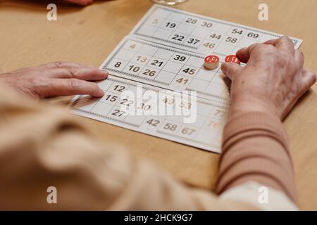 Over the shoulder view of hands of unrecognizable aged man sitting at wooden table and playing board game Stock Photo
