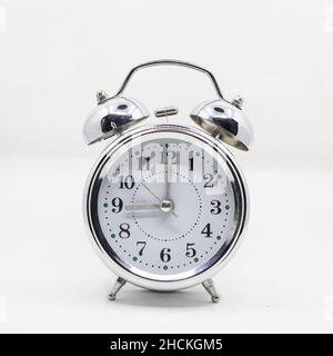 a vintage classic ringing alarm clock with a silver body and white analog round dial isolated in a white background Stock Photo
