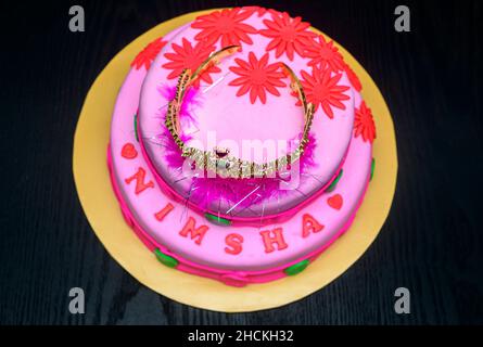 Beautiful home-baked two-tier wedding party cake design with a tiara on top, decorated with icing flowers. Delicious pink-red color-themed round cake Stock Photo