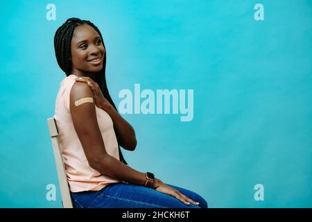Vaccinated attractive young woman smiling with plaster on hand right after getting covid-19 vaccine shot, looking sideway at copy space Stock Photo