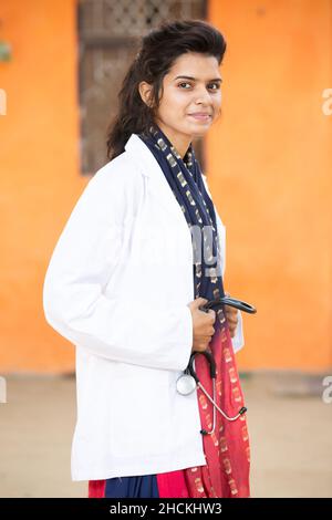 Portrait Of Young Smiling indian Female Doctor holding Stethoscope Standings looking at camera with positive emotions against orange background. healt Stock Photo