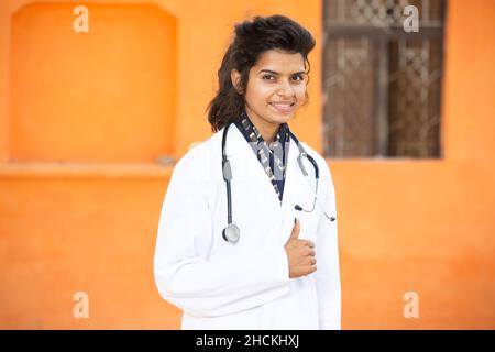 Portrait Of Young Smiling indian Female Doctor Wearing Stethoscope and Apron Standing do thumbs up, She is looking at camera with positive emotions ag Stock Photo