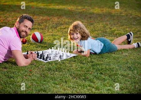 Happy family outdoor. Father and son playing chess in spring garden. Child learning to play chess. Little boy think or plan chess game. Checkmate. Stock Photo