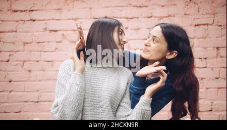 Portrait of two young pretty Indian girls playing a peek a boo against a brick wall background Stock Photo