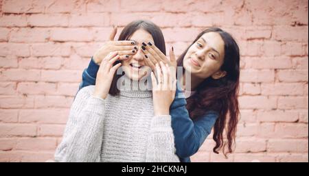 Portrait of two young pretty Indian girls playing a peek a boo against a brick wall background Stock Photo