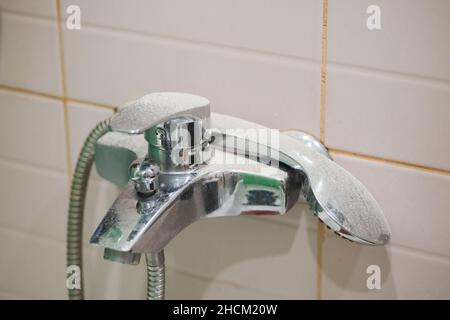 Dirt and dust on faucet and shower head because of renovation works in bathroom with tiled pinkish wall in background. Renovation process causing dirt Stock Photo