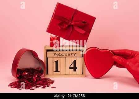 cropped view of woman holding heart-shaped metallic box near presents and calendar on pink Stock Photo