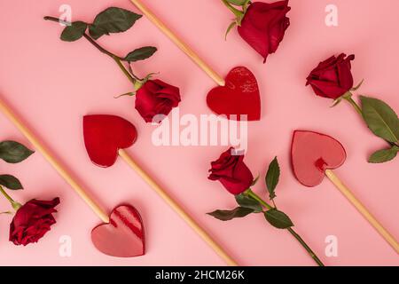 flat lay of heart-shaped lollipops near red roses on pink Stock Photo