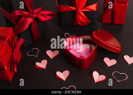 paper cut hearts near metallic box and wrapped presents on black Stock Photo