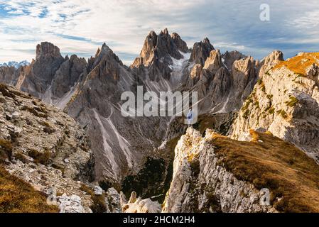 Lonely hiker on a rocky ledge in front of the Cadini di Misurina mountain massif in the Sexten Dolomites at sunrise, South Tyrol, Italy Stock Photo