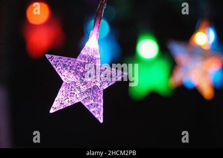 Simple graphic shot of star shaped multicoloured lights on a Christmas tree. Close up with one star in detail and others blurred Stock Photo