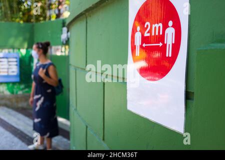 Red sign attached to green wall informing people to keep 2 meter social distance due to COVID-19 pandemic,prevention and protection from Coronavirus Stock Photo