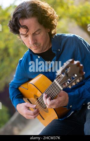 Middle-aged man playing Spanish guitar sitting on park bench Stock Photo