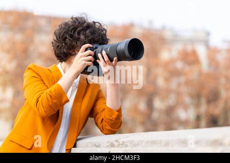 Young brunette woman with curly hair taking a picture with telephoto lens Stock Photo