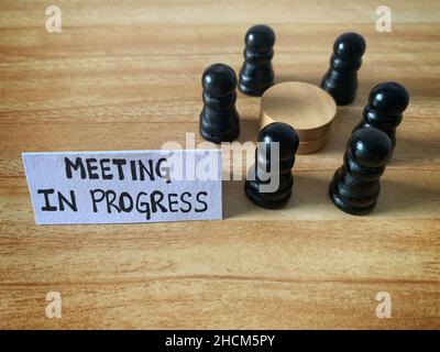 Meeting in progress text on a paper note with chess pawn circling a round table. Meeting concept. Stock Photo