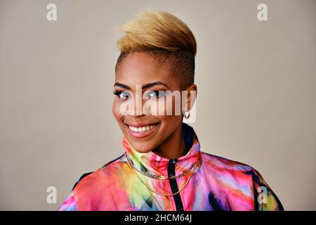 Happy Stylish Female Hipster with cool trendy short hair, jewelry and colorful jacket Against Ivory Background Stock Photo