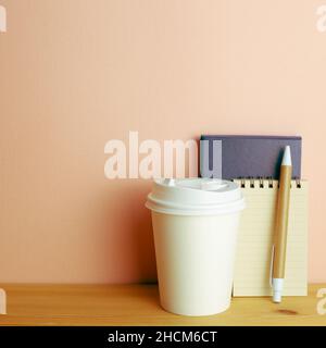 Notebook, pen, paper coffee cup on wooden desk. pink wall background. workspace Stock Photo