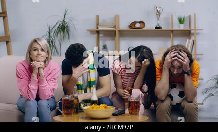 frustrated football fans sitting with bowed heads near beer and chips at home Stock Photo