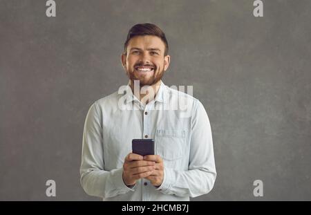 Happy young man using smartphone and smiling standing isolated on grey background Stock Photo