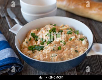 Seafood salad in a bowl made with salmon fillet, boiled eggs, onions, mayonnaise and chives. Served with fresh baguette on wooden table Stock Photo