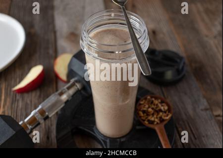 Fitness breakfast shake with whey protein powder, homemade granola and fresh fruits. Served in a shaker on a table with dumbbell Stock Photo