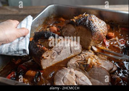 Fresh cooked roasted pork with gravy and vegetables in a roasting pan. Served by a woman´s hand Stock Photo