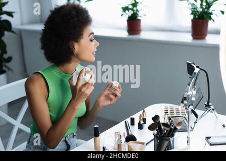 Side view of african american blogger spraying perfume near cosmetics and smartphone at home Stock Photo