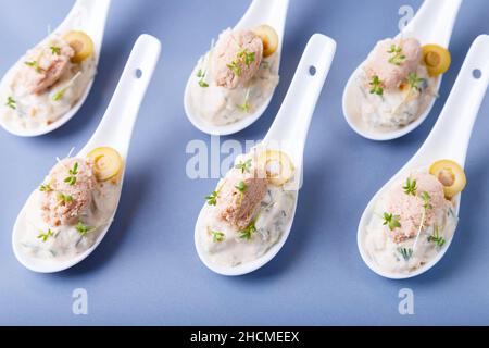 Cold appetizer made from cod liver, cod caviar, olives, cucumber and microgreens on serving spoons. Traditional cold dish. Close-up, blue plate, black Stock Photo