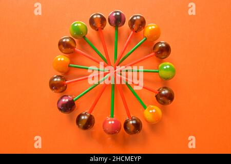 Various colorful lollipops on pastel background. Bright juicy colored lollipops on an orange background. Lollipops in the form of a flower. Fruit cand Stock Photo