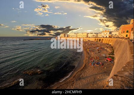 Gallipoli, Puglia, Italy. August 2021. The sandy beach in the old town is packed with people bathing and sunbathing. Golden hour. Stock Photo