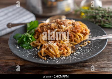 Traditional spaghetti bolognese served on a dark plate on rustic and wooden table background with fork Stock Photo