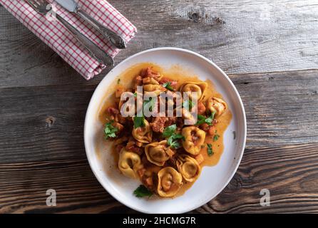Tortellini in a delicious pancetta, tomato, vegetable sauce. Served on a white plate on rustic and wooden table background with copy space Stock Photo