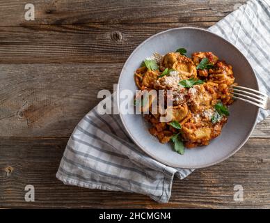Vegetarian pasta dish with tortellini filled with cheese and served in a delicious vegetable tomato sauce with parmesan cheese on wooden table Stock Photo