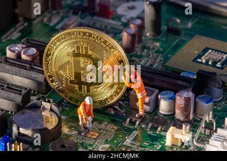 Bitcoin mining inside a computer. Two small Bitcoin miners figurines extracting valuable electronically-mined digital cryptocurrency from motherboard Stock Photo