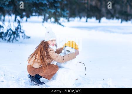 Cute little teenage girl having fun playing making snowman in the snowy winter forest. Snow games. Winter vacation. Stock Photo