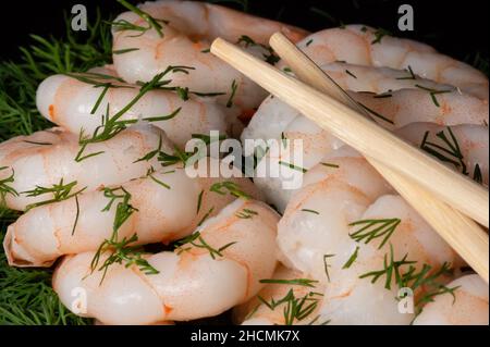 Close up view of freshly cooked peeled prawns or shrimps and chopsticks on dark background. Stock Photo
